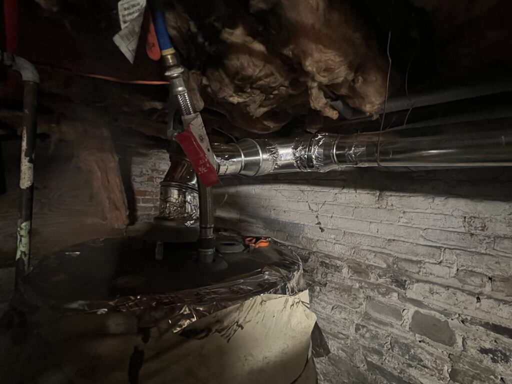 Basement water line with flexible supply hoses and a red-handled ball valve along an old brick foundation