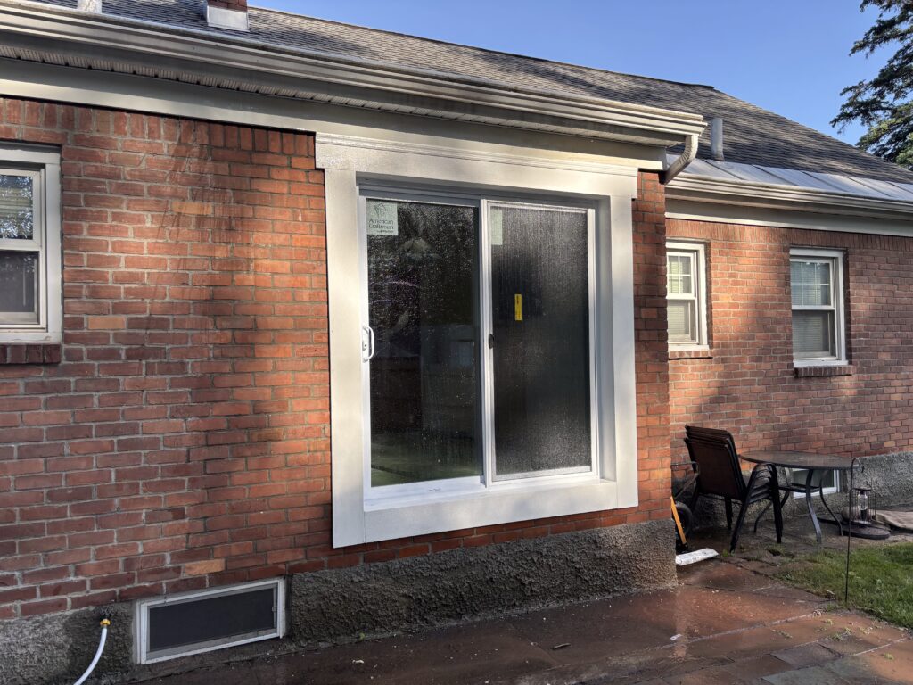 New white sliding patio door with wide white trim set into the brick wall of a ranch house