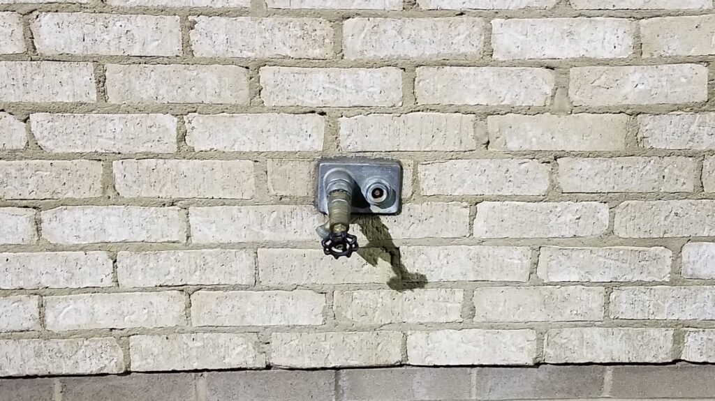 Wall-mounted outdoor faucet on a tan brick wall
